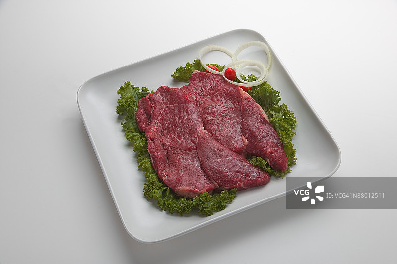 托盘上的未煮熟西冷牛排配生菜、洋葱和番茄装饰图片素材