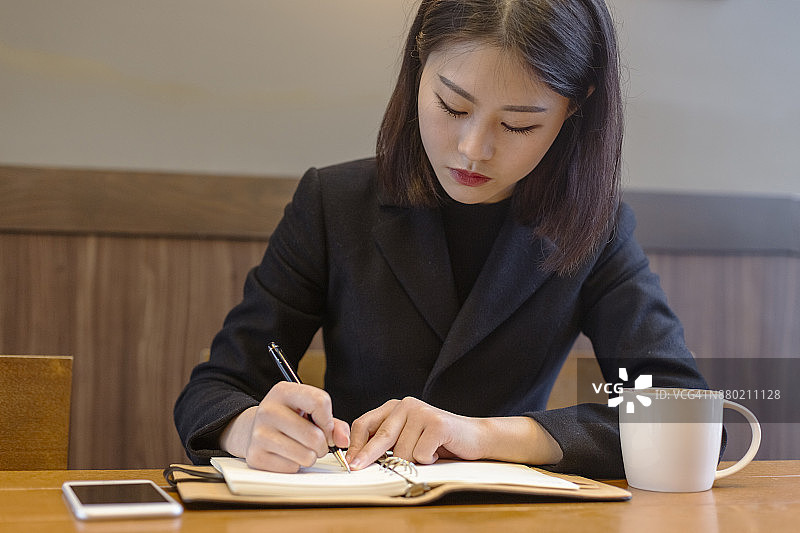 在咖啡馆的桌旁做笔记的职业女性图片素材