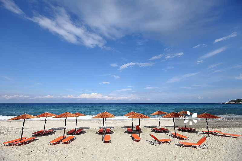 希腊空旷海滩上蓝色多云天空下的沙滩伞图片素材