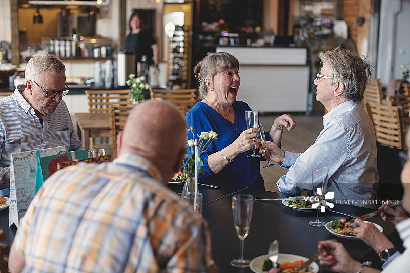 老年夫妇在餐厅与朋友共进午餐，举杯庆祝图片素材