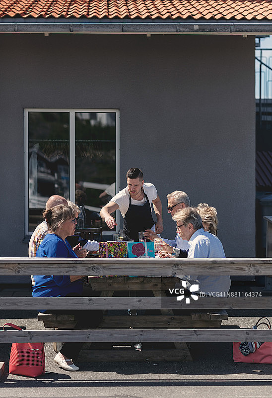 年轻的男服务员在餐厅外为年长的朋友提供食物图片素材