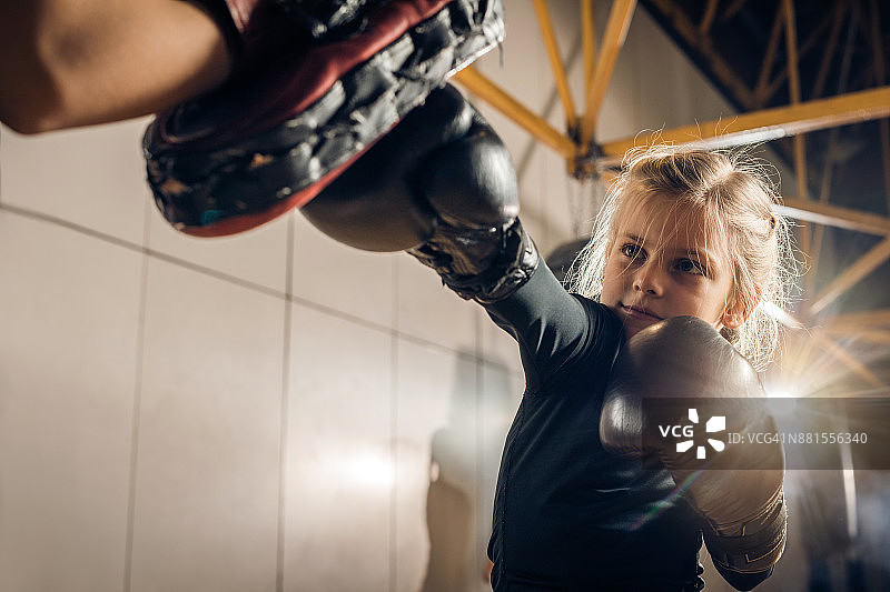 一位小拳击手在健身房与一位无法辨认的教练进行体育训练图片素材