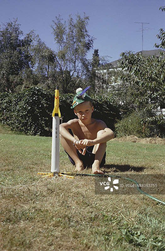 男孩坐在后院的玩具火箭旁图片素材