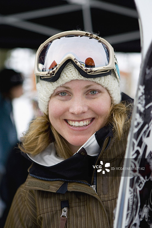 笑容满面的女人拿着滑雪板，穿着滑雪服图片素材