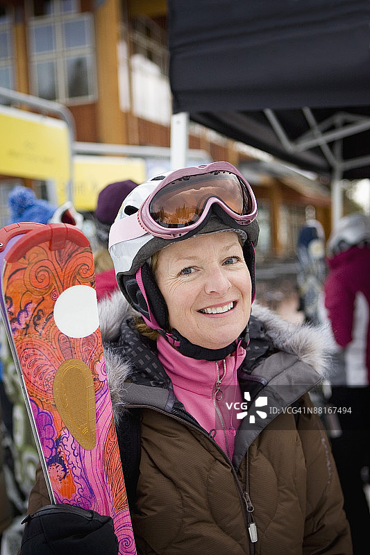 笑容满面的女人拿着滑雪板，穿着滑雪服图片素材
