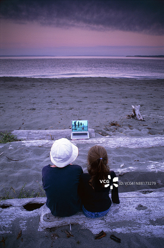 孩子们坐在沙滩浮木上使用笔记本电脑图片素材