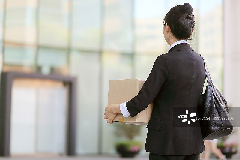 被解雇的女商人站在办公室外的纸箱旁图片素材