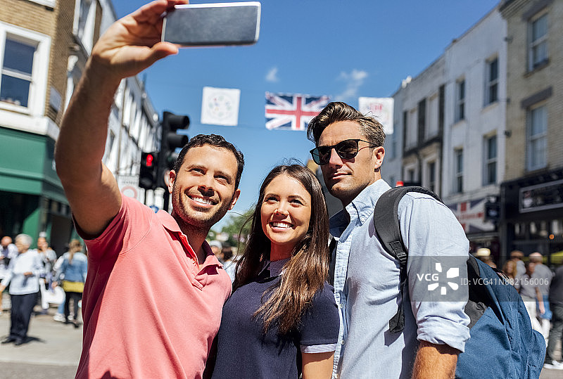 英国伦敦波多贝罗路：三个朋友用智能手机自拍的肖像图片素材