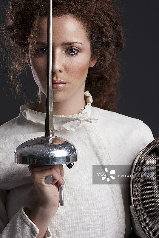 击剑运动比赛：深灰色背景，运动型女性，卷发红发女击剑运动员肖像图片素材