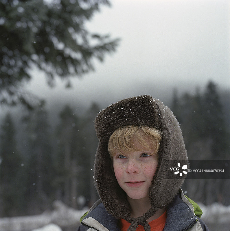 戴着毛皮衬里帽子的男孩在雪林里图片素材