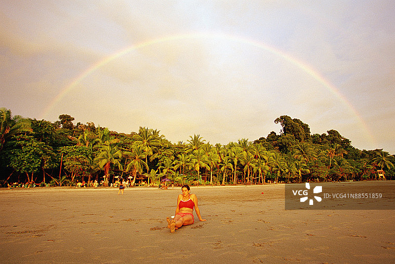 彩虹下坐在海滩上的女人，位于哥斯达黎加曼努埃尔·安东尼奥国家公园图片素材