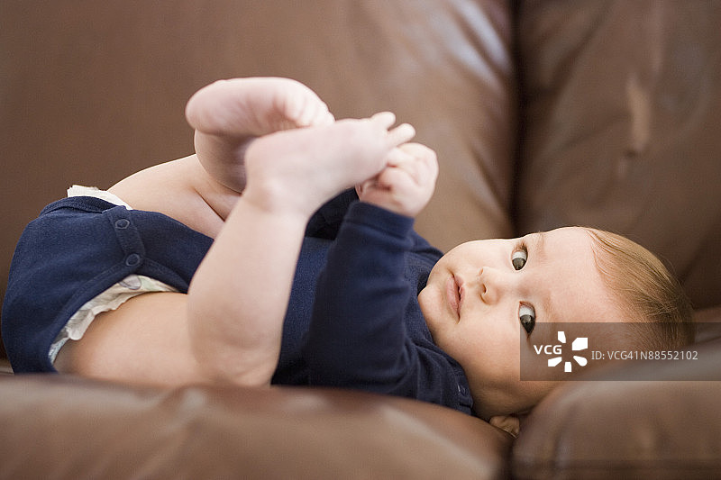 躺在沙发上抱着脚的男婴图片素材