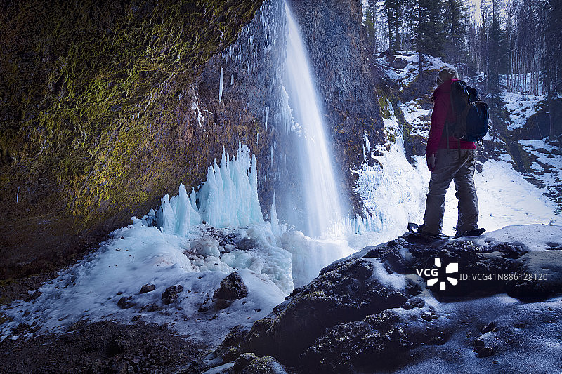 一名穿着雪鞋的人在加拿大不列颠哥伦比亚省韦尔斯格雷省立公园的冰冻穆尔瀑布后方进行探索图片素材