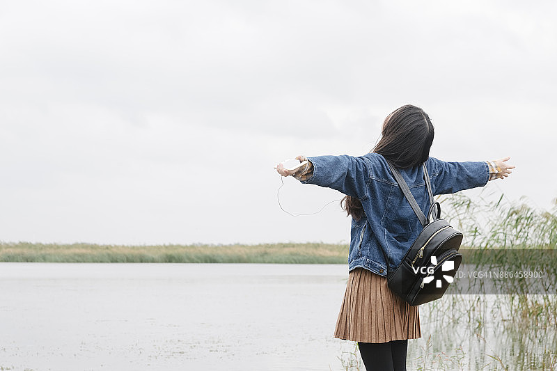 在湖边伸开双臂的年轻女子的背影图片素材