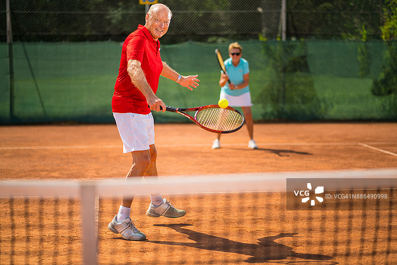 老年人在红土球场上进行户外双打比赛图片素材