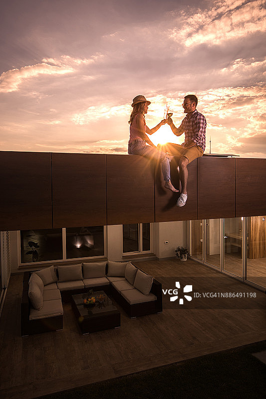 坐在屋顶上在日落时分敬酒的年轻情侣图片素材