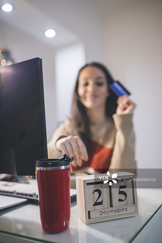 在圣诞树旁用信用卡的快乐年轻女人图片素材