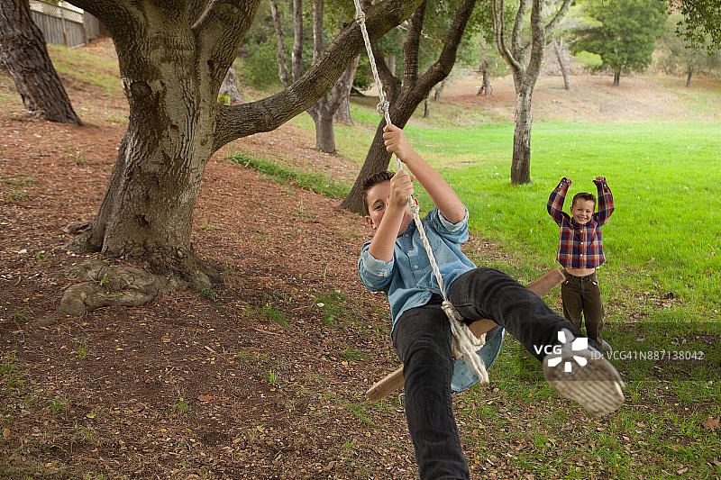 在户外自然公园里，弟弟推着哥哥荡秋千图片素材
