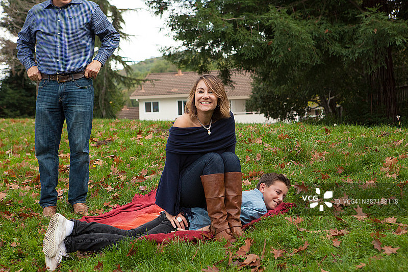 母亲和儿子在公园的毯子上休息，父亲在背景中图片素材