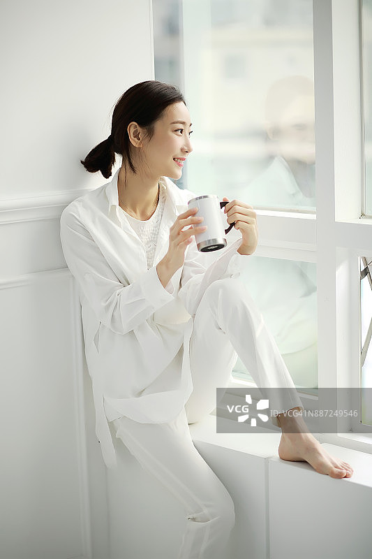 年轻女人坐在窗台上，端着咖啡杯图片素材