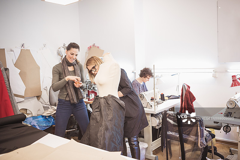 服装设计师协同工作。两位女裁缝在时装设计工作室为时装模特设计服装图片素材
