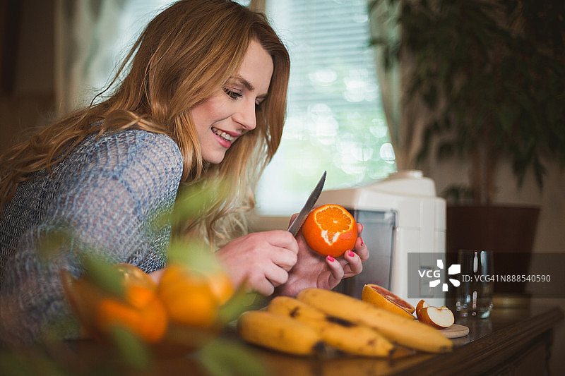 年轻女人在厨房用电动榨汁机制作冰沙图片素材
