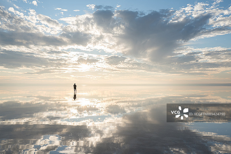 男人站在盐湖上，欣赏日落云彩图片素材