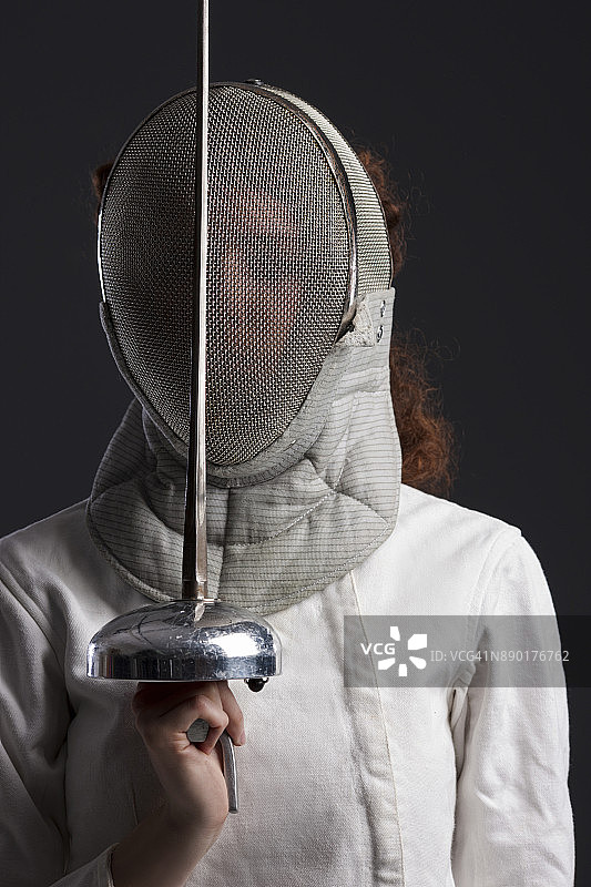 击剑运动比赛：深灰色背景，运动型女性，卷发红发女击剑运动员肖像图片素材