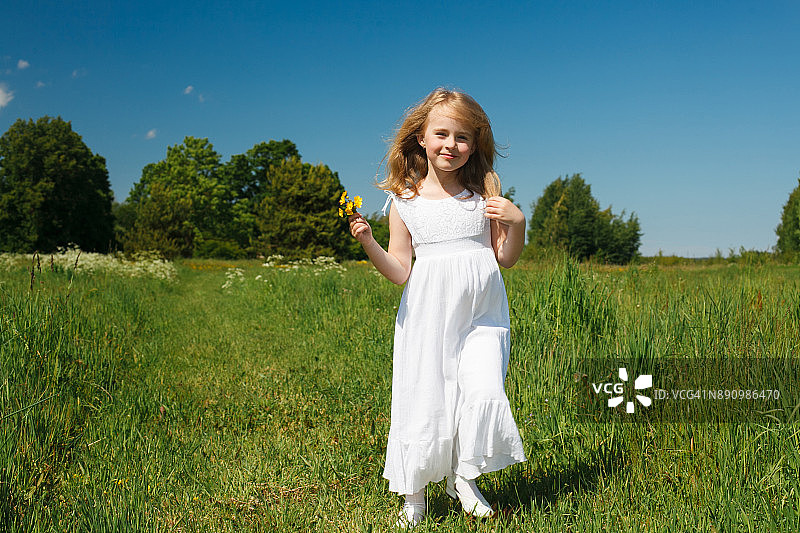 在开满野花的夏日田野上，身穿白色连衣裙的长发小女孩图片素材