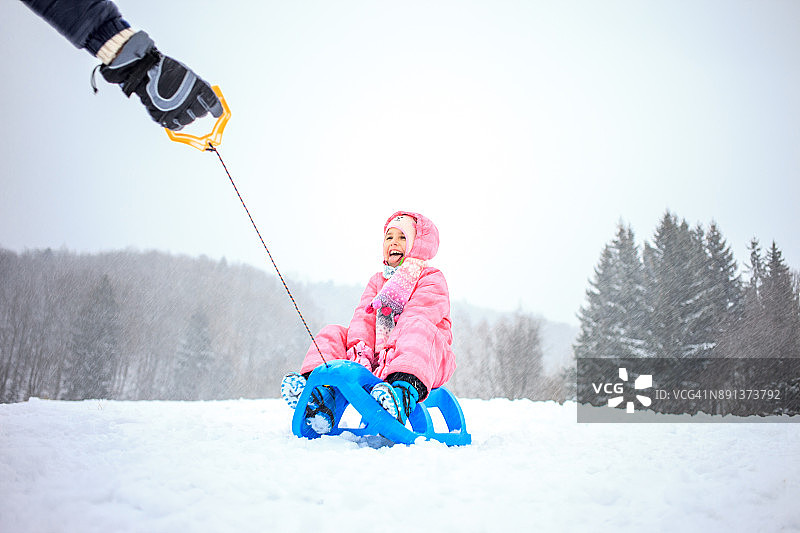 父亲拖着女儿在雪橇上图片素材