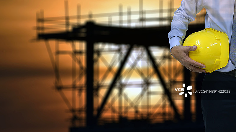 安全施工概念：安全工程师手持黄色安全帽，装载机在后图片素材