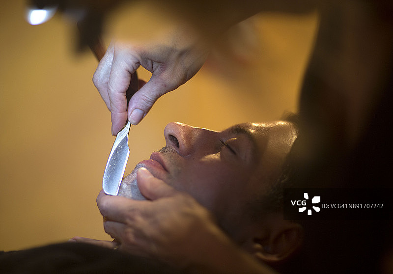 在男士理发店里为男人刮胡子的女人图片素材