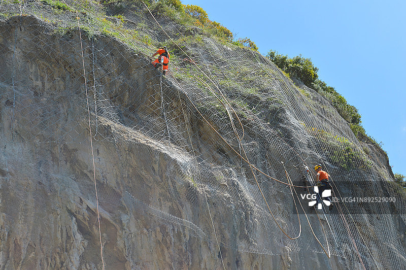 在意大利阿马尔菲山上的防护网上进行绳降作业的两名工人图片素材