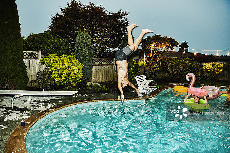夏季晚间派对：男子后空翻跳入泳池，朋友们观看图片素材