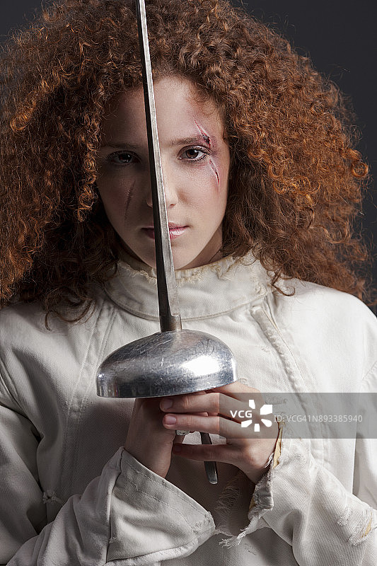 击剑运动比赛：深灰色背景，运动型女性，卷发红发女击剑运动员肖像图片素材