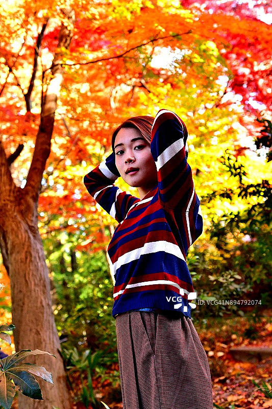 在东京色彩鲜艳的枫树下摆姿势的年轻日本女性图片素材