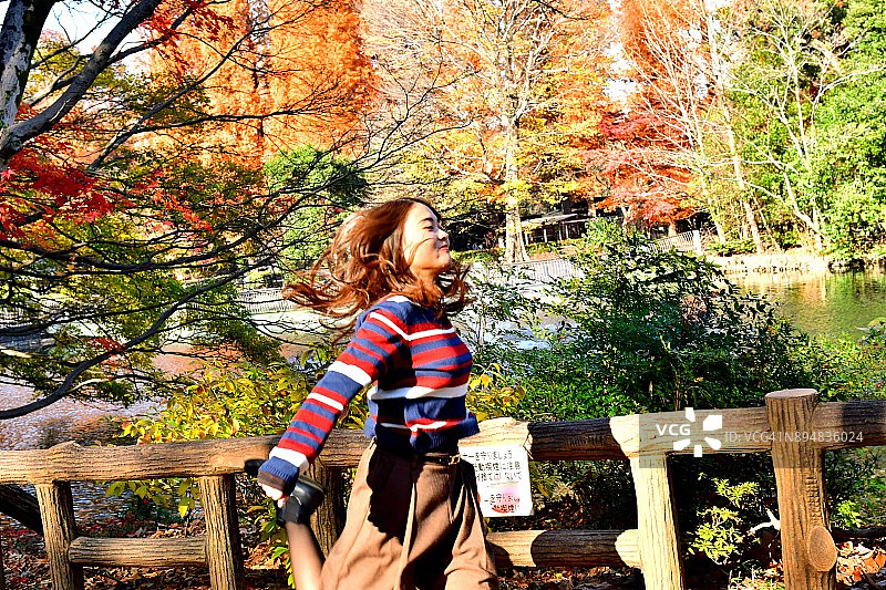 在东京井之头公园秋色中摆姿势/跳跃的年轻日本女子图片素材