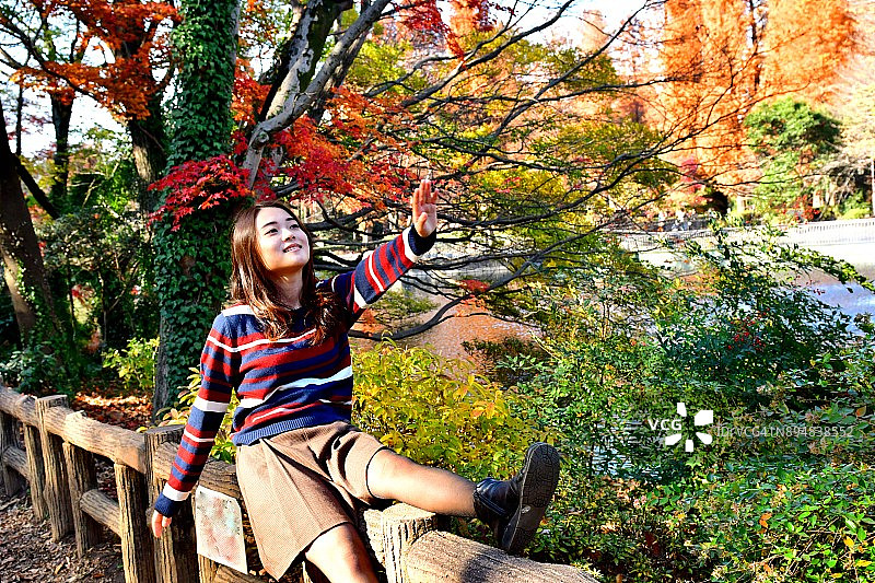 在东京井之头公园秋色中摆姿势/跳跃的年轻日本女子图片素材