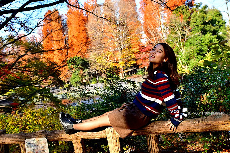 在东京井之头公园秋色中摆姿势/跳跃的年轻日本女子图片素材