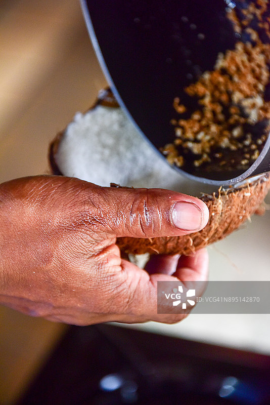 将椰子油从锅中倒入半个椰子壳中，锅里有加热过的椰肉图片素材