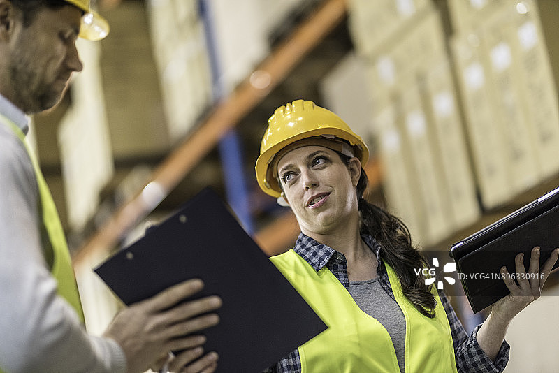 仓库工人向女同事展示笔记图片素材