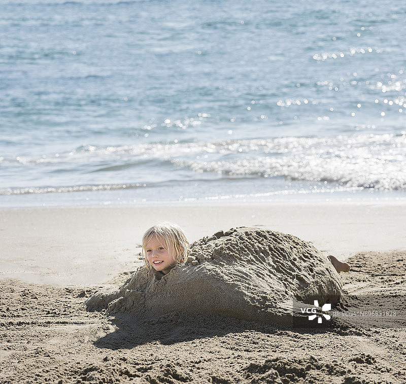 在海滩上戴着沙制乌龟壳的男孩图片素材