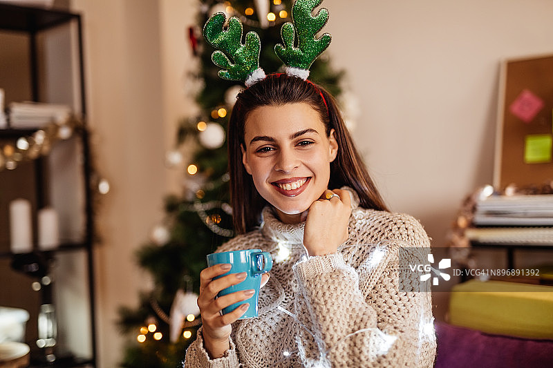 圣诞节期间，女人在圣诞树背景下喝咖啡图片素材