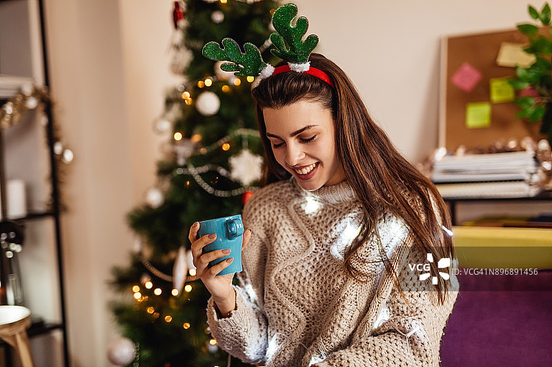 圣诞节期间，女人在圣诞树背景下喝咖啡图片素材
