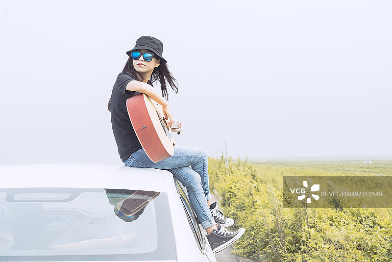 天空下时尚女孩车顶弹吉他图片素材