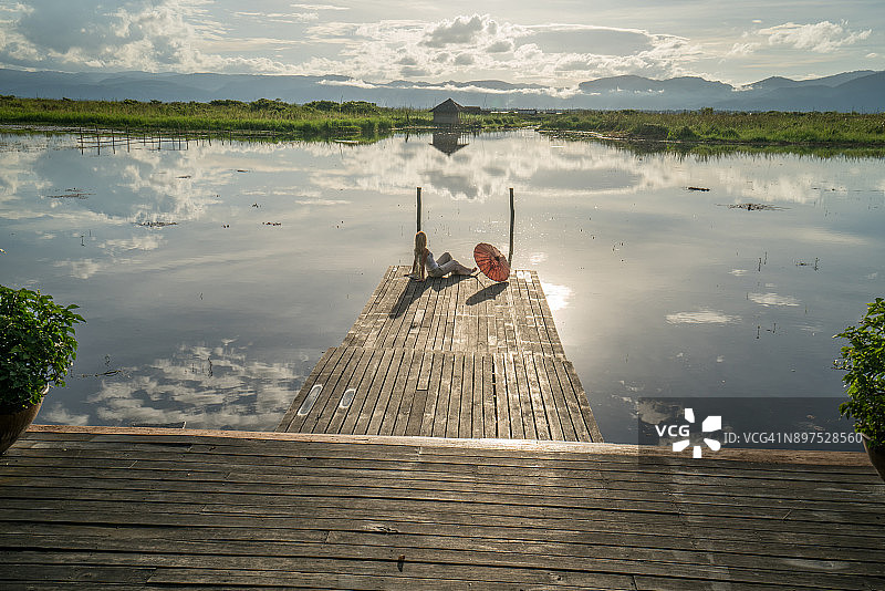 年轻女人在缅甸日出时分的湖边码头上放松图片素材