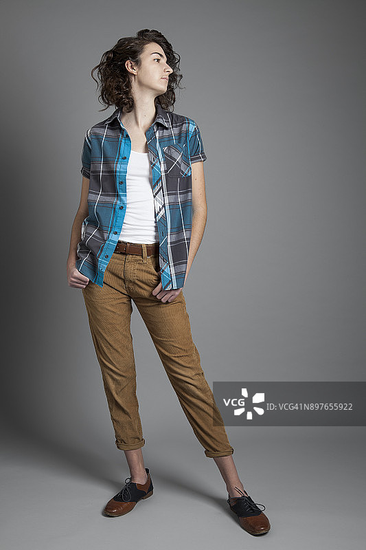 十几岁的女孩站在灰色背景前，在工作室里穿着蓝色格子衬衫，侧脸轮廓图片素材