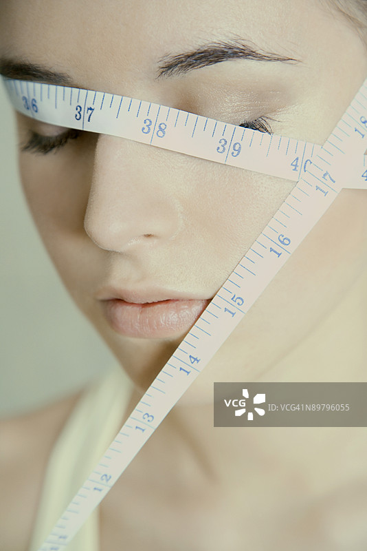 闭眼的女性脸上缠绕着卷尺图片素材