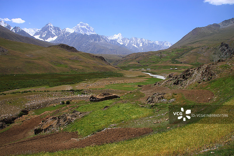 乡村泥屋：背景是郁郁葱葱的绿色山谷和白雪皑皑的山脉图片素材