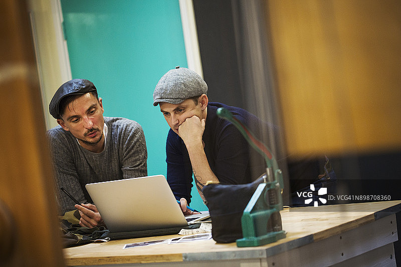 两名男子在裁缝店工作室看笔记本电脑屏幕图片素材